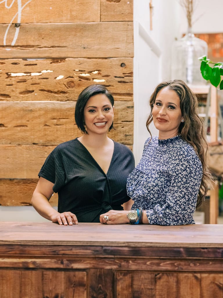 Two women smiling behind a wooden counter